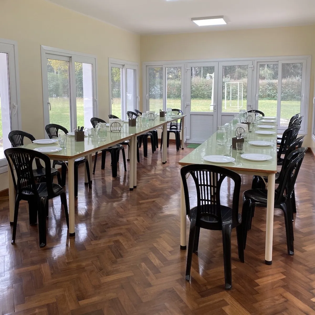 Bright communal dining room with long tables set for shared meals overlooking the gardens